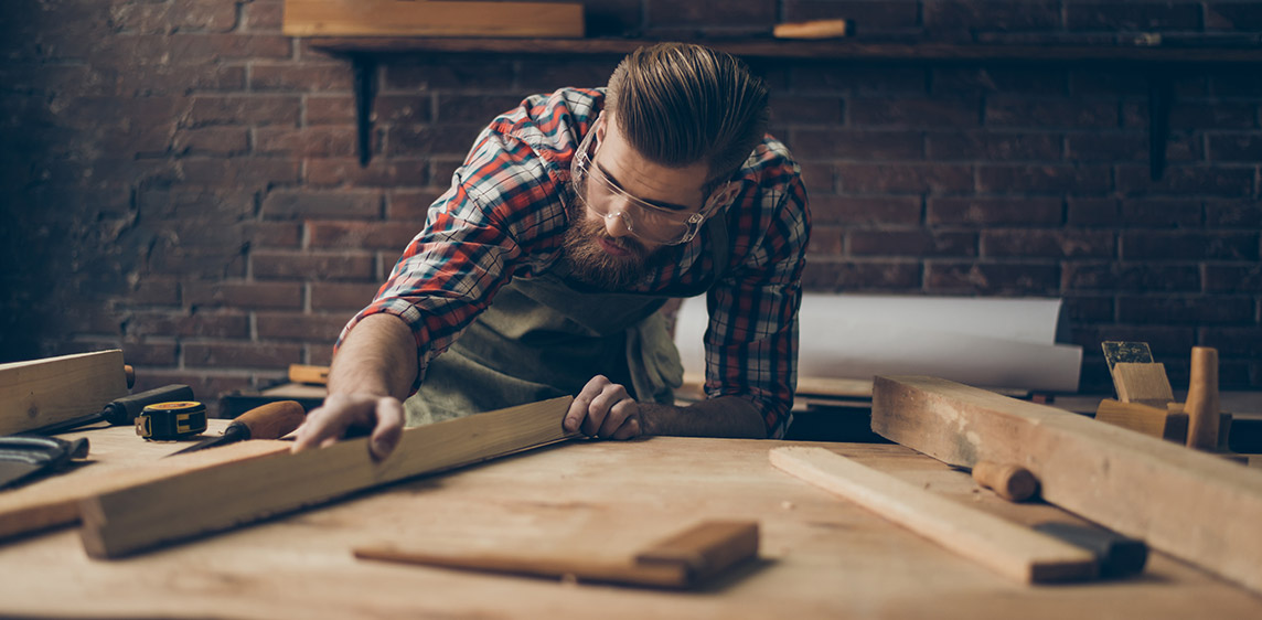 Gesundheit in Beruf und Umwelt Ein Handwerker bearbeitet ein Stück Holz in seiner Werkstatt.